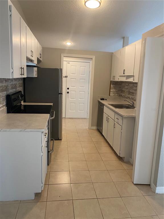 A galley-style kitchen features white cabinets, stainless steel appliances, and light-colored tile flooring — 2459 LANDOVER BOULEVARD, SPRING HILL, FL