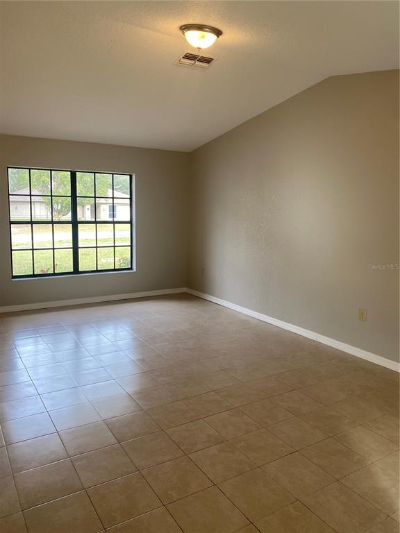 An empty room features beige walls, a large grid window, and light-colored tiled flooring — 2459 LANDOVER BOULEVARD, SPRING HILL, FL