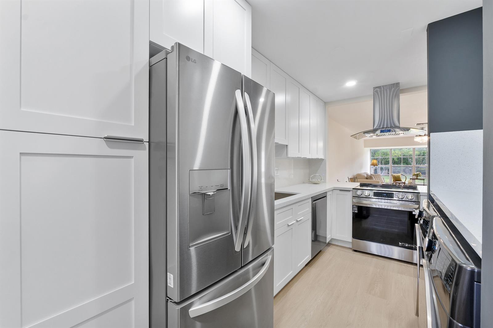 A modern kitchen features white cabinetry, stainless steel appliances, and light wood-look flooring — 1030 Citrus Way # 204, Delray Beach FL 33445, DELRAY BEACH, FL