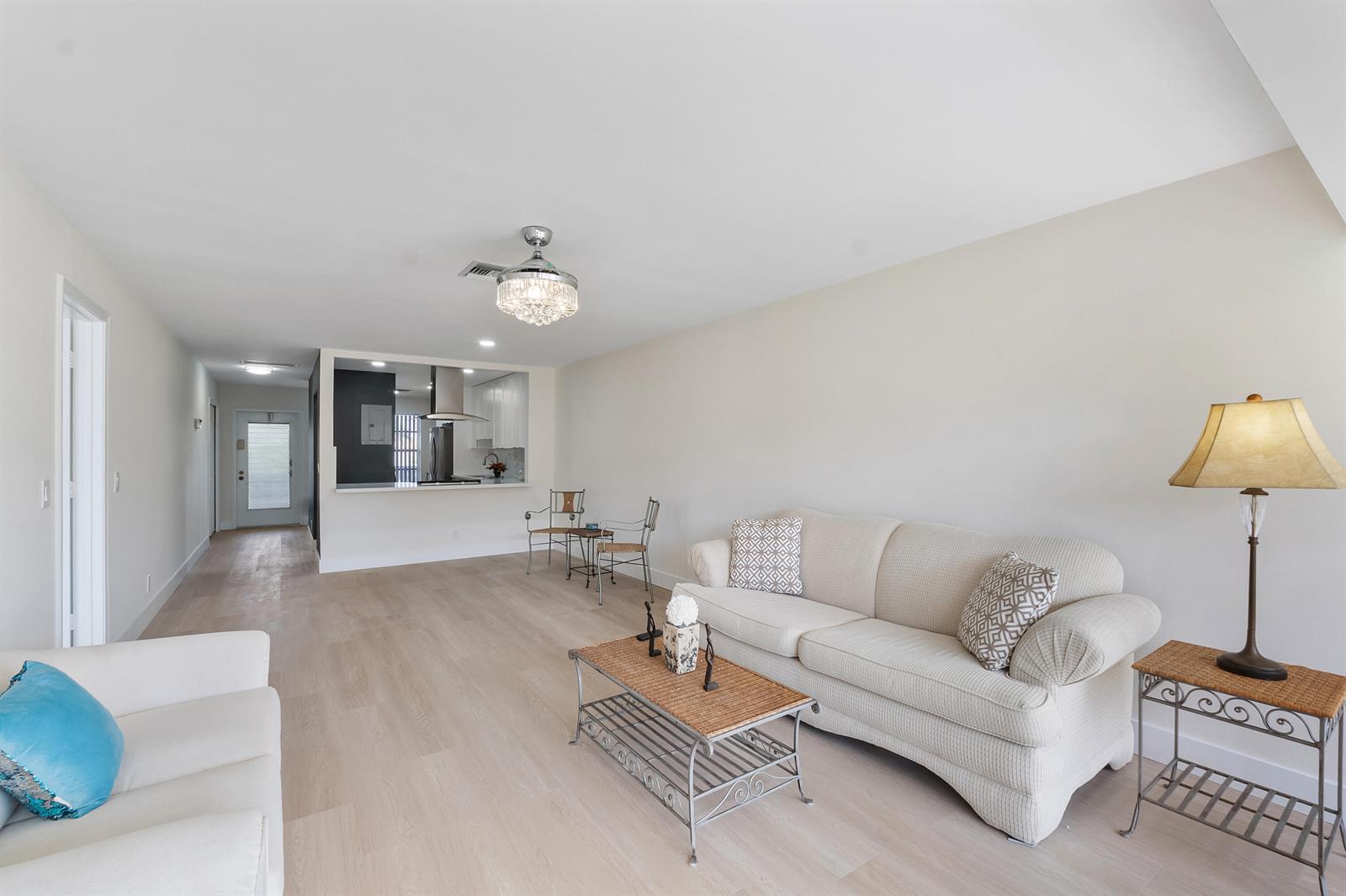 A living room with light wood flooring, a beige sofa, and an open kitchen view — 1030 Citrus Way # 204, Delray Beach FL 33445, DELRAY BEACH, FL
