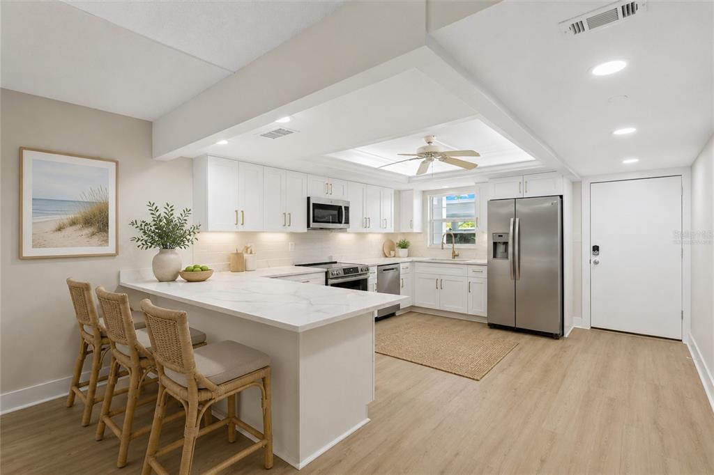 A modern kitchen features white cabinetry, stainless steel appliances, a breakfast bar, and light flooring — 5600 BEACH WAY DRIVE UNIT 109, SARASOTA, FL