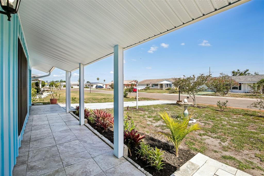 A covered tiled porch overlooks a front yard with landscaping and a residential street — 704 OJAI AVENUE, SUN CITY CENTER, FL