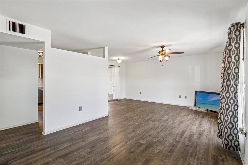 A living room with white walls, wood-look flooring, a ceiling fan, and a television — 704 OJAI AVENUE, SUN CITY CENTER, FL