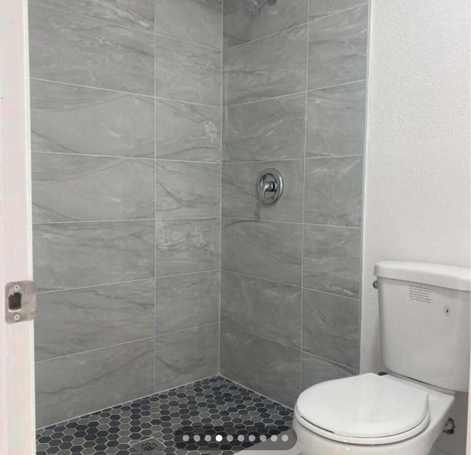 A bathroom features a walk-in shower with gray tile walls and a dark hexagonal floor — 952 30th Street, West Palm Beach FL 33407, WEST PALM BEACH, FL