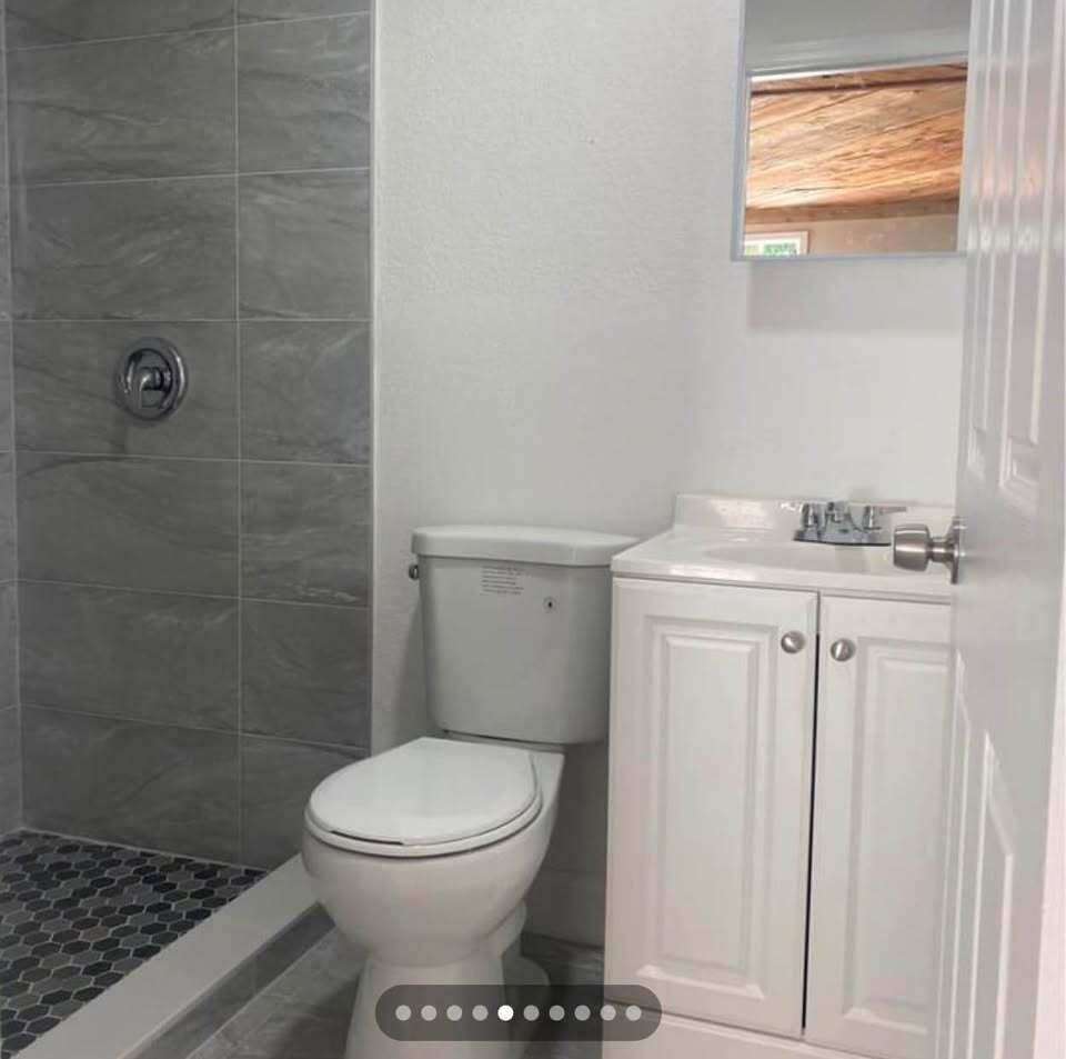 A small bathroom features a walk-in shower with gray tile, a white toilet, and a vanity — 952 30th Street, West Palm Beach FL 33407, WEST PALM BEACH, FL