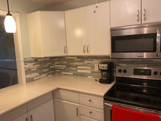 A kitchen features white cabinets, a stainless steel microwave, a stove, and a tiled backsplash — 5100 SW 64th Ave # 202, Davie FL 33314, DAVIE, FL