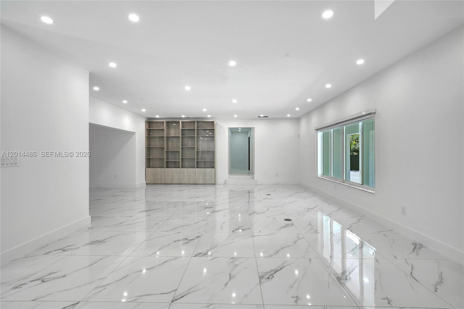 A spacious room features white marble floors, recessed lighting, and a large built-in wooden bookshelf — 711 Sunset Dr, Coral Gables FL 33143, CORAL GABLES, FL