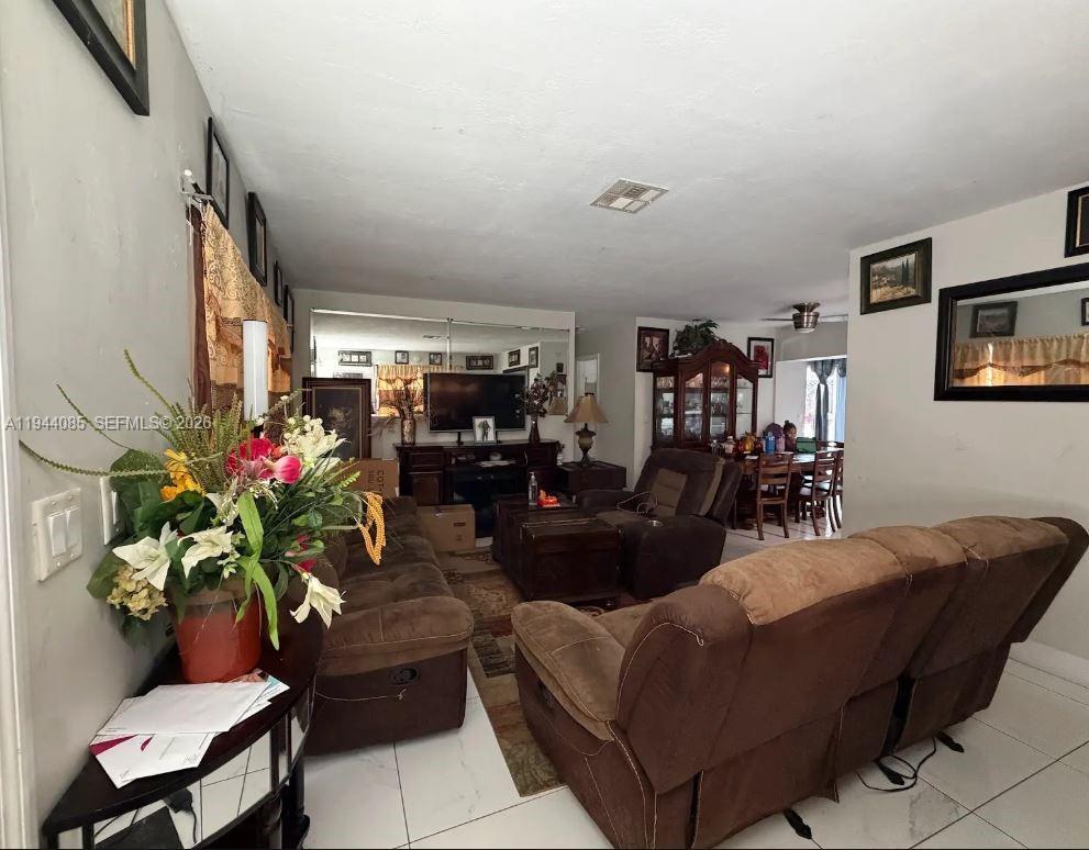 A living room features brown reclining sofas, a mirrored wall, and white tile flooring — 7570 Miramar Pkwy, Miramar FL 33023, MIRAMAR, FL