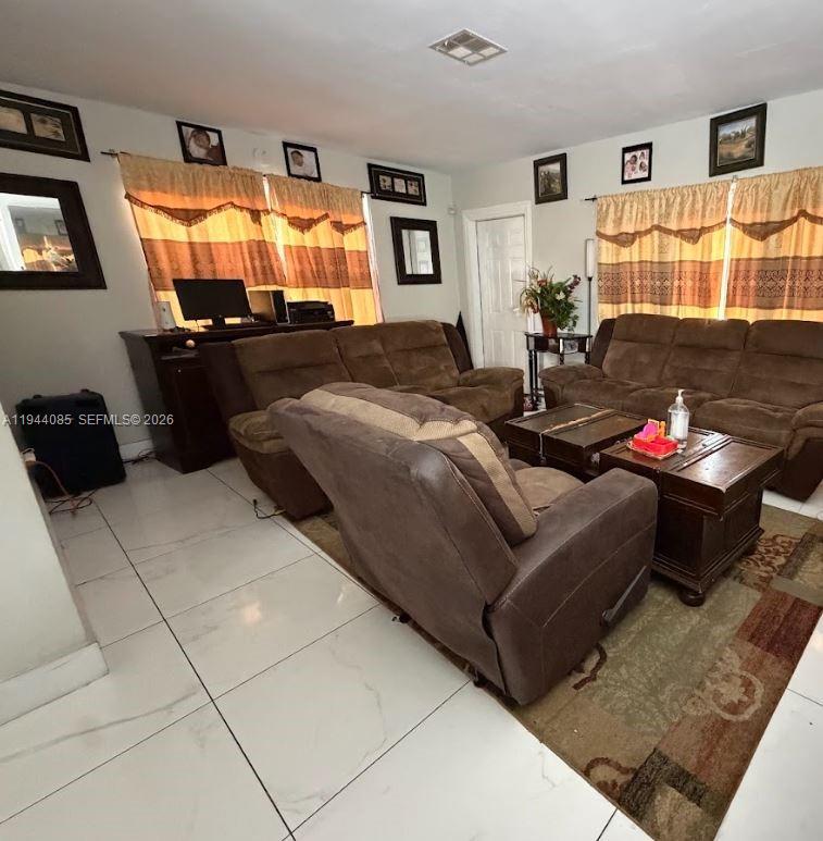 A living room features brown sofas, a coffee table, tile flooring, and window curtains — 7570 Miramar Pkwy, Miramar FL 33023, MIRAMAR, FL