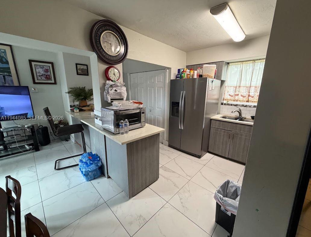 A kitchen features light-colored tile flooring, gray cabinetry, stainless steel appliances, and a breakfast bar — 7570 Miramar Pkwy, Miramar FL 33023, MIRAMAR, FL