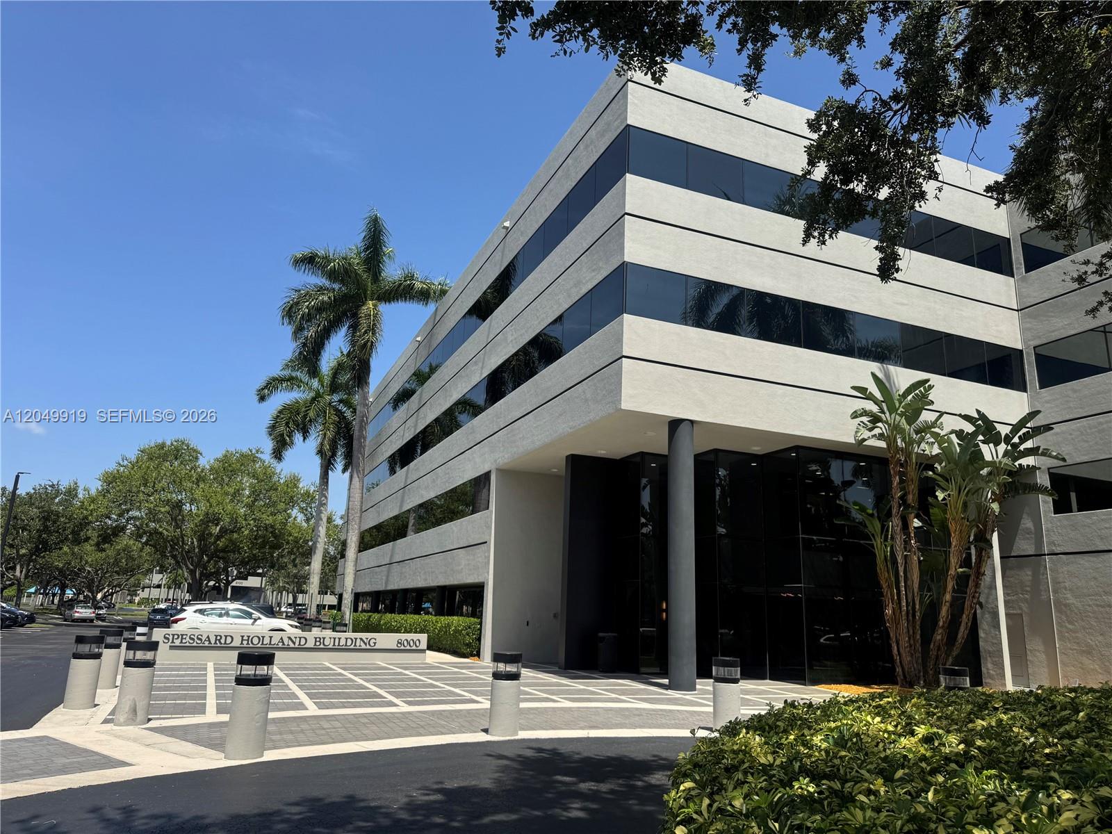 A multi-story office building features a modern facade with horizontal glass windows and palm trees — MIAMI LAKES, FL