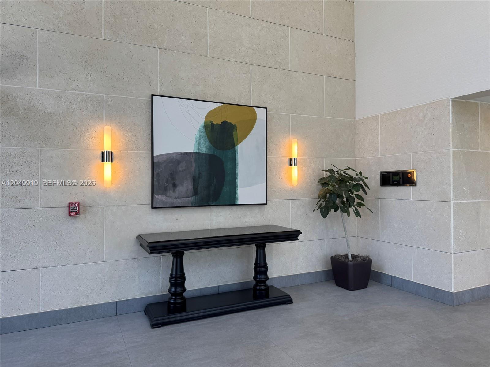 A modern lobby features a stone wall with a console table, artwork, and wall sconces — MIAMI LAKES, FL