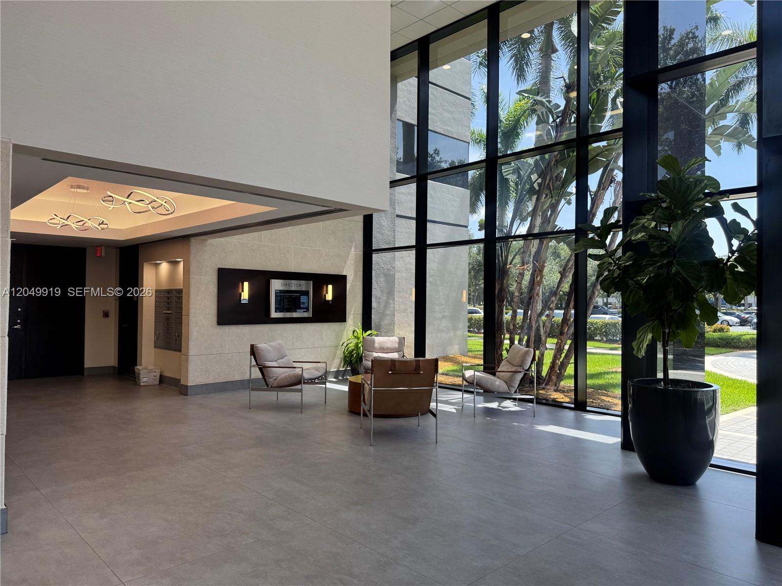 A modern lobby features floor-to-ceiling windows, tiled floors, contemporary seating, and a digital directory — MIAMI LAKES, FL