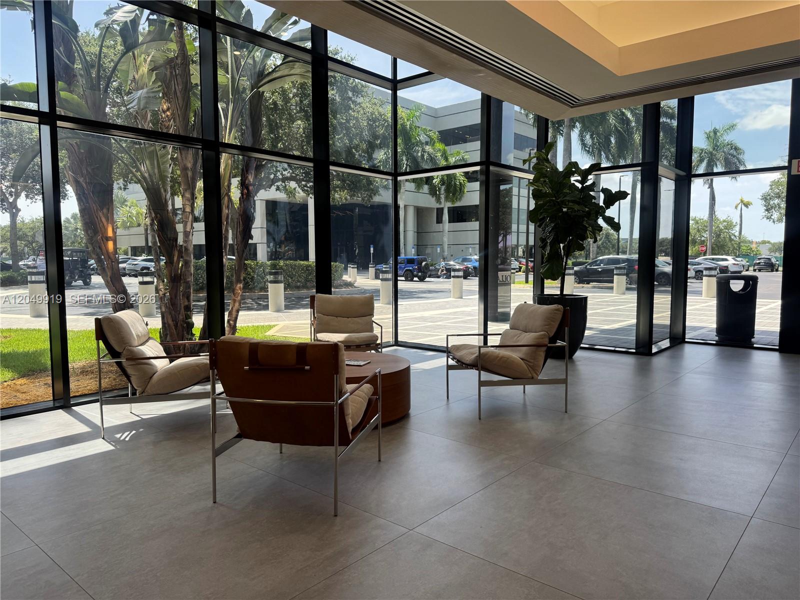 A modern lobby features floor-to-ceiling windows, tile flooring, and a seating area with armchairs — MIAMI LAKES, FL