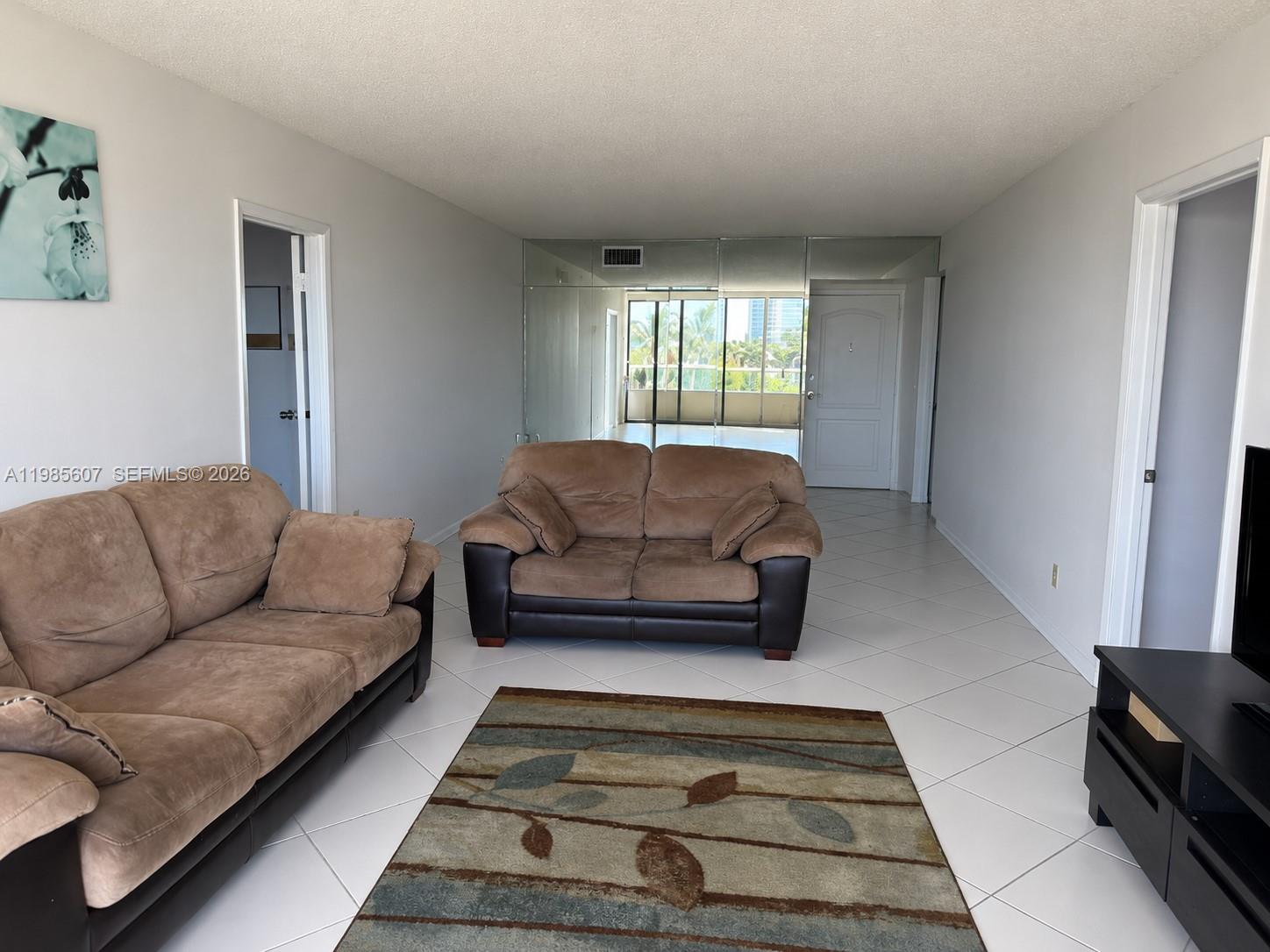 A living room features light tile floors, two brown sofas, and a mirrored accent wall — 3675 N Country Club Dr # 508, Aventura FL 33180, AVENTURA, FL