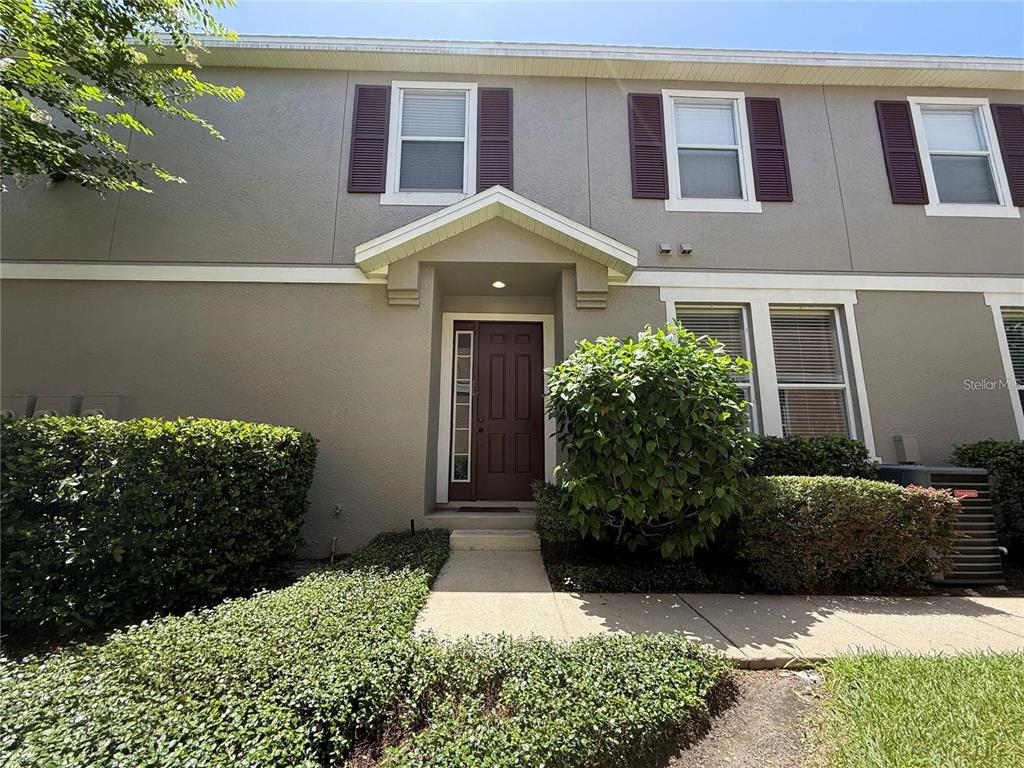 A two-story townhouse exterior features a brown front door, shuttered windows, and landscaped bushes — 10238 CALA LILY TRAIL UNIT S, ORLANDO, FL