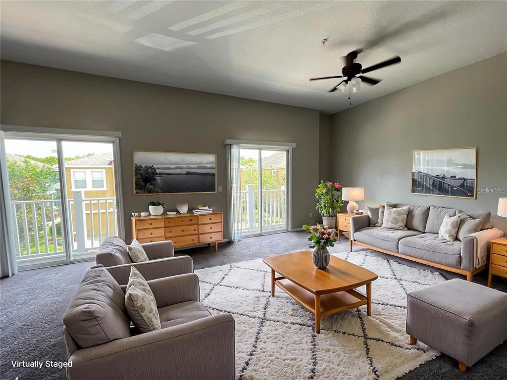 A living room with gray sofas, a wooden coffee table, and two sliding glass doors — 10238 CALA LILY TRAIL UNIT S, ORLANDO, FL