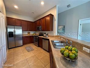 A kitchen features dark wood cabinets, stainless steel appliances, and a tan countertop with a sink — 10238 CALA LILY TRAIL UNIT S, ORLANDO, FL