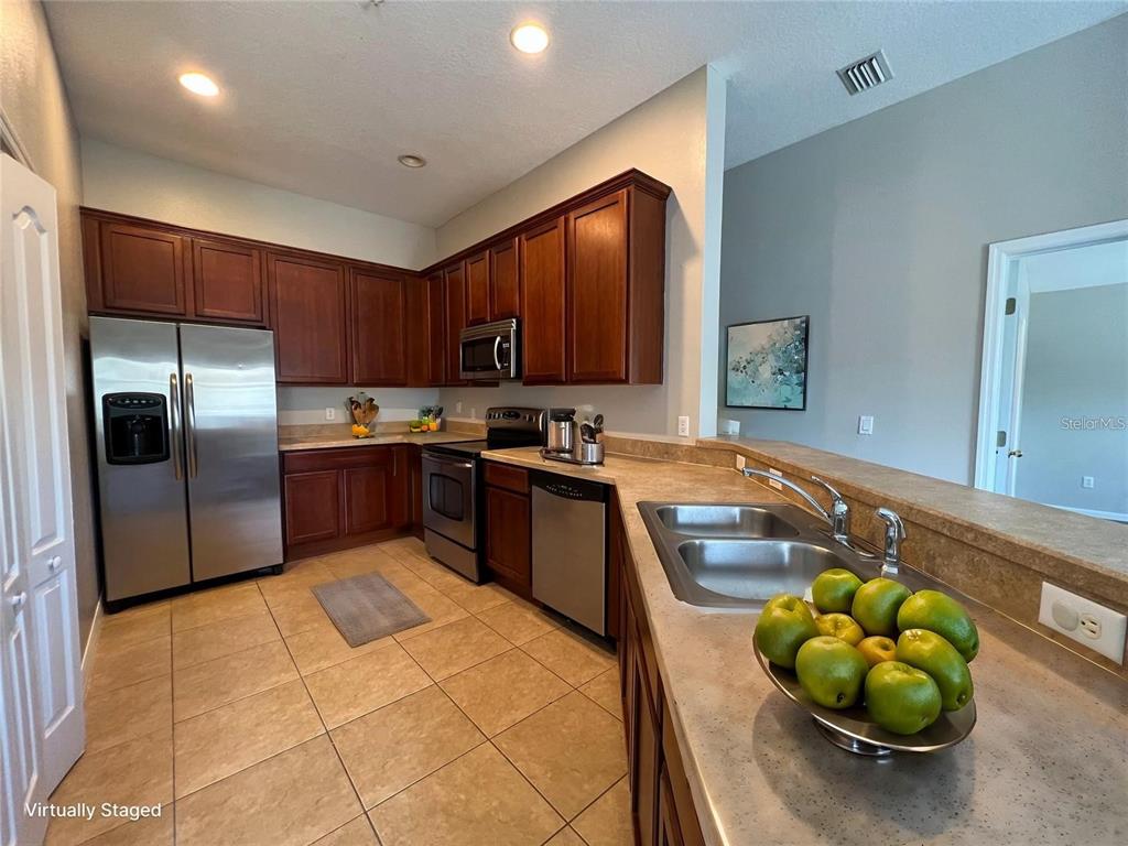 A kitchen features wood cabinets, stainless steel appliances, tile flooring, and a double sink — 10238 CALA LILY TRAIL UNIT S, ORLANDO, FL