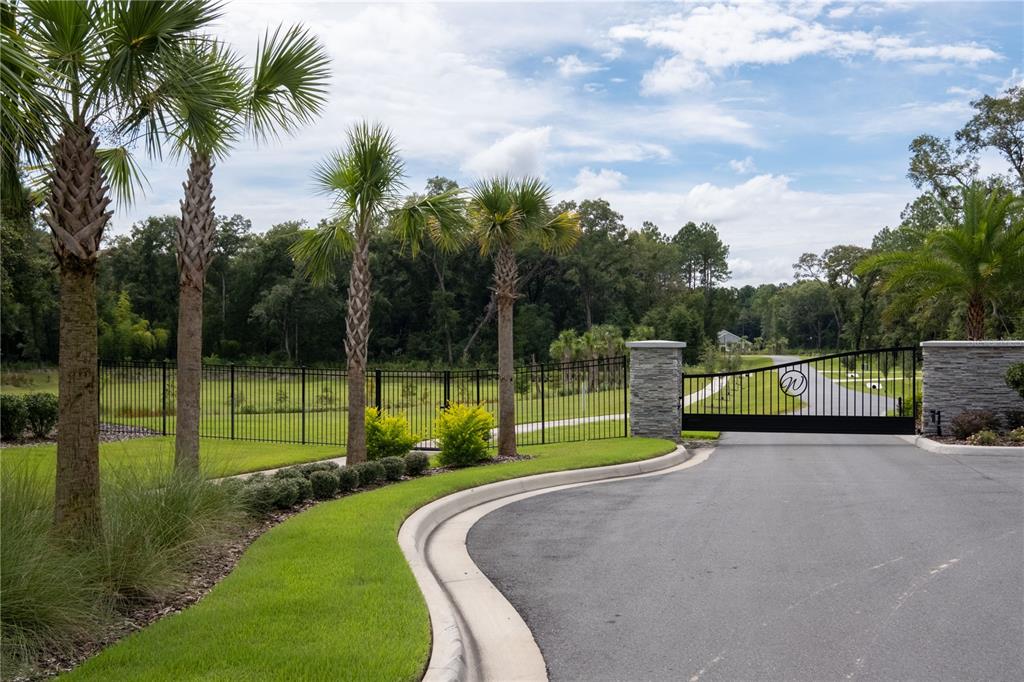 A gated entrance with stone pillars, palm trees, and a black metal fence — 12387 SW 16TH LANE, NEWBERRY, FL