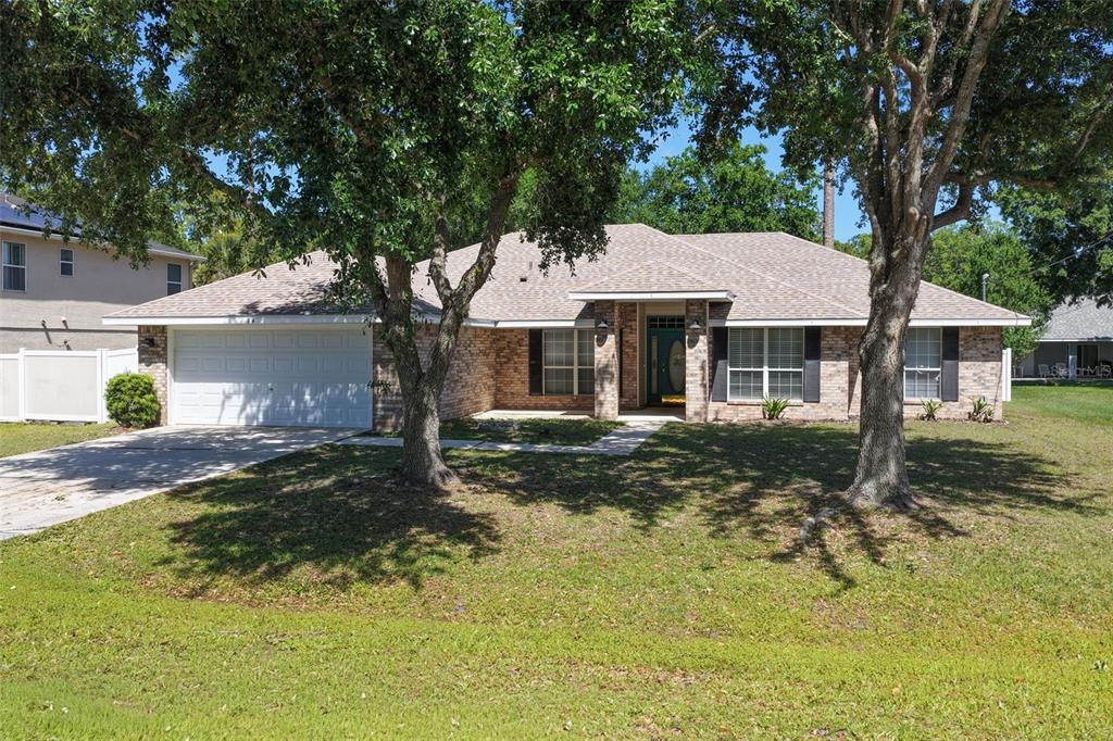A single-story brick house with a two-car garage and mature trees in the front yard — 84 BRUNSWICK LANE, PALM COAST, FL
