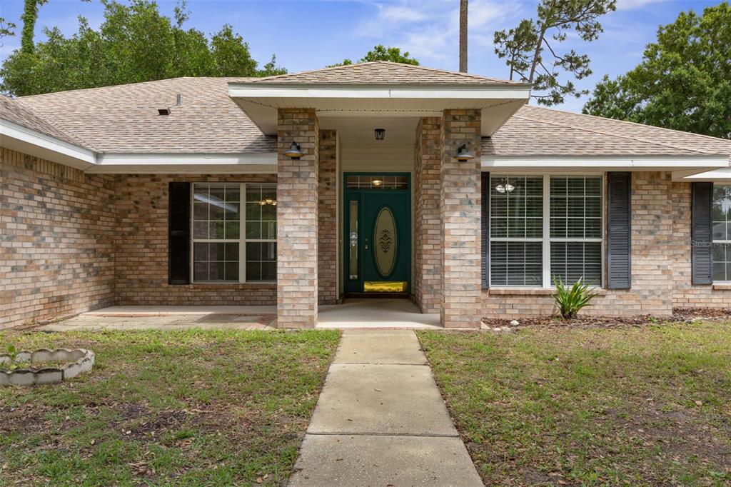 A single-story brick house features a covered entryway with a teal front door and walkway — 84 BRUNSWICK LANE, PALM COAST, FL