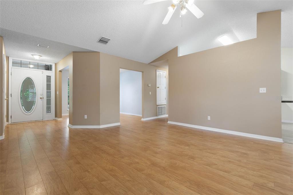 An empty living room features light wood-look flooring, beige walls, and a vaulted ceiling — 84 BRUNSWICK LANE, PALM COAST, FL