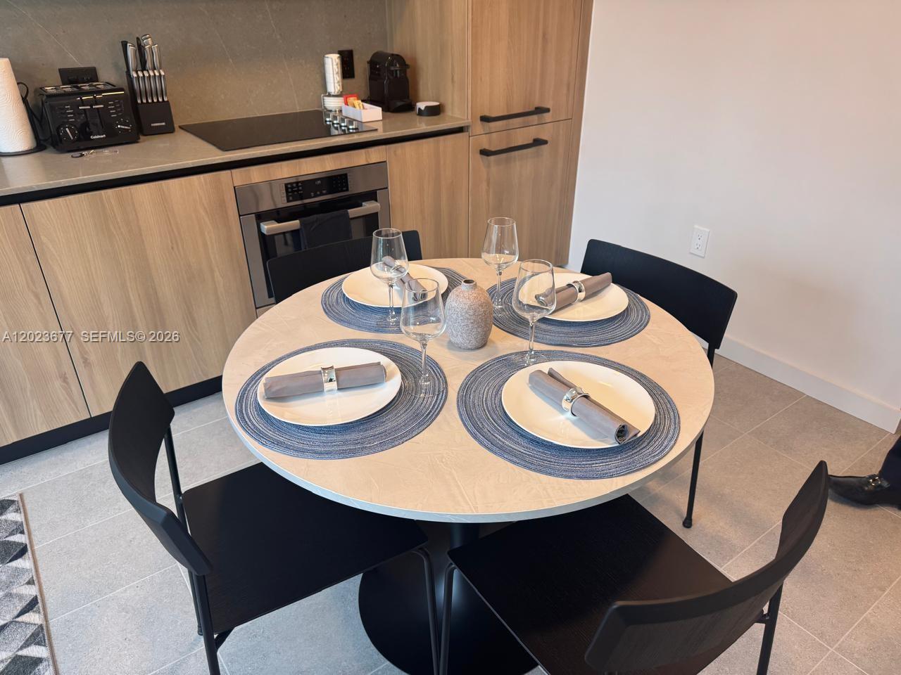 A round dining table with four place settings sits in a kitchen with wood cabinetry — 121 NE 5th St # 2102, Miami FL 33132, MIAMI, FL