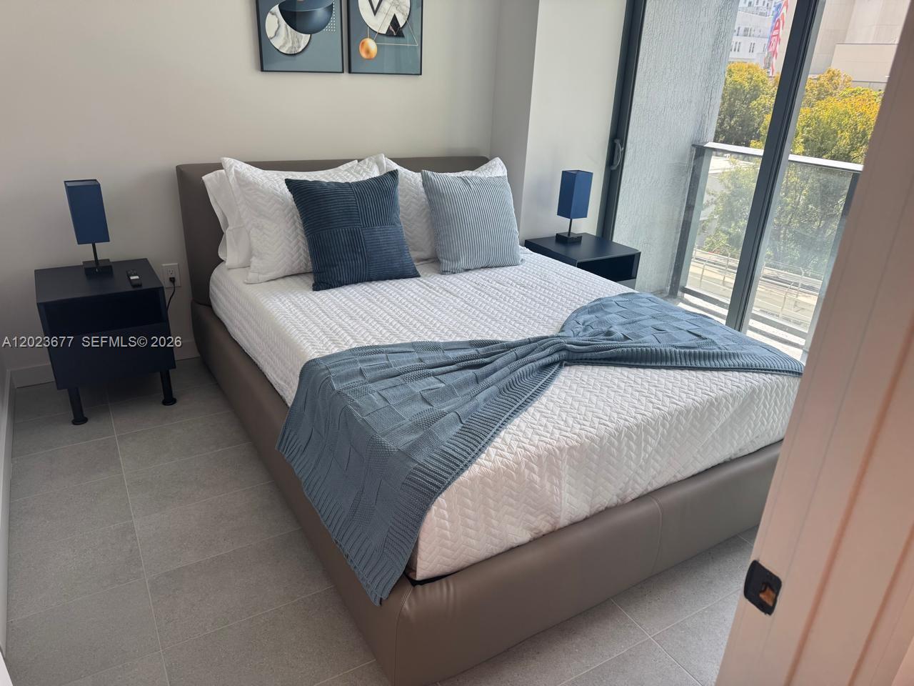 A bedroom features a bed with blue accents, two nightstands, and a balcony with trees — 121 NE 5th St # 2102, Miami FL 33132, MIAMI, FL