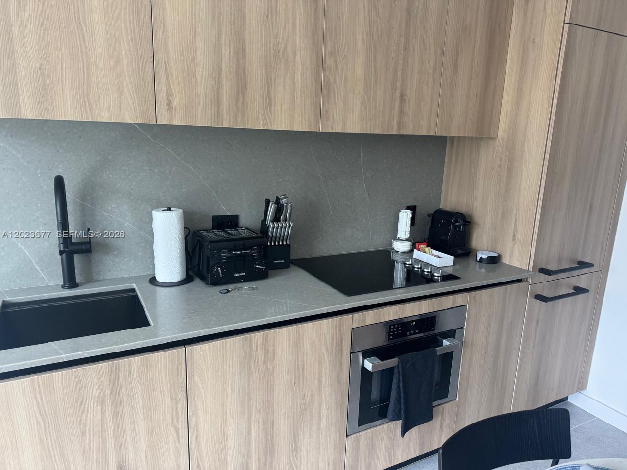 A modern kitchen features light wood cabinets, a grey stone backsplash, and stainless steel appliances — 121 NE 5th St # 2102, Miami FL 33132, MIAMI, FL