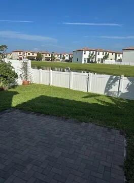A paved patio overlooks a grassy backyard, a white vinyl fence, and a small pond — 3016 King Palm Way, Riviera Beach FL 33410, RIVIERA BEACH, FL