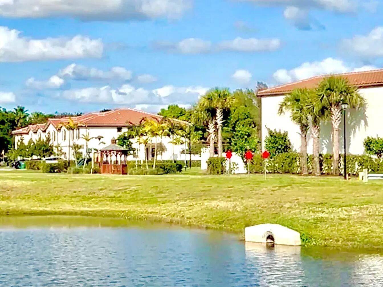 A pond sits in front of a grassy lawn with palm trees and two buildings — 3016 King Palm Way, Riviera Beach FL 33410, RIVIERA BEACH, FL