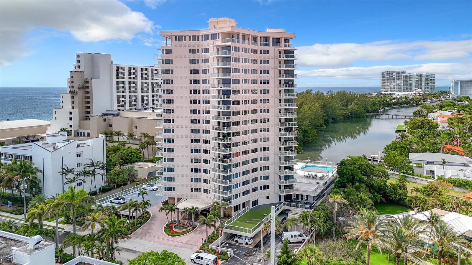 An aerial view shows a tall, light-colored residential high-rise building situated between the ocean and a canal — 3000 Holiday Drive # 1505, Fort Lauderdale FL 33316, FORT LAUDERDALE, FL