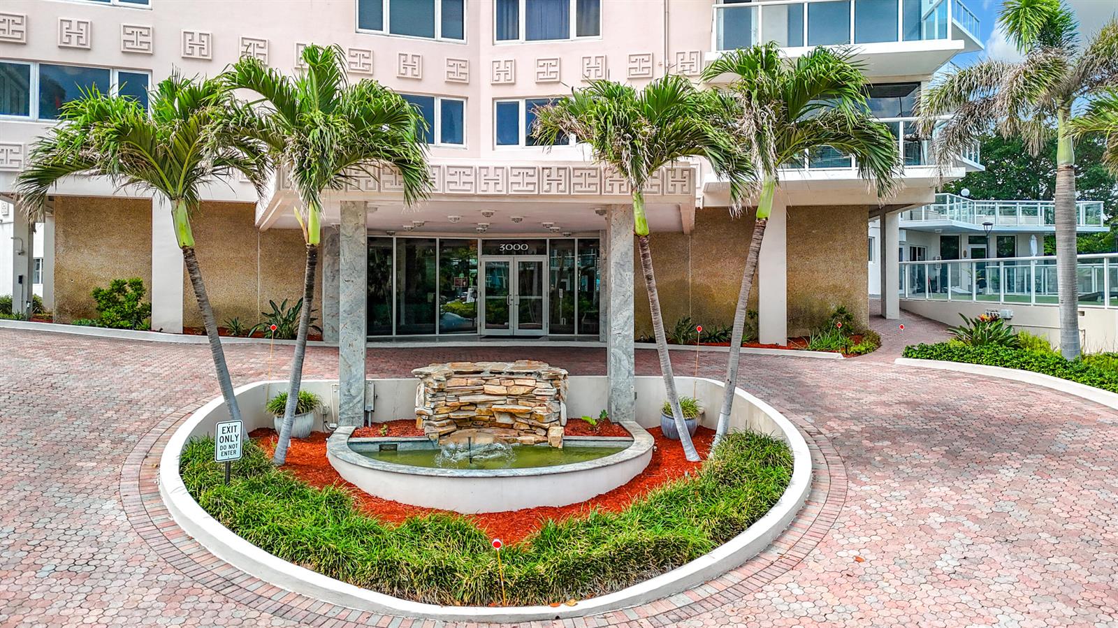 The exterior of a building features a circular driveway with a central fountain and palm trees — 3000 Holiday Drive # 1505, Fort Lauderdale FL 33316, FORT LAUDERDALE, FL