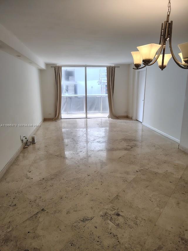 An empty living room features polished stone tile flooring, a chandelier, and sliding glass doors — 6039 Collins Ave # 407, Miami Beach FL 33140, MIAMI BEACH, FL