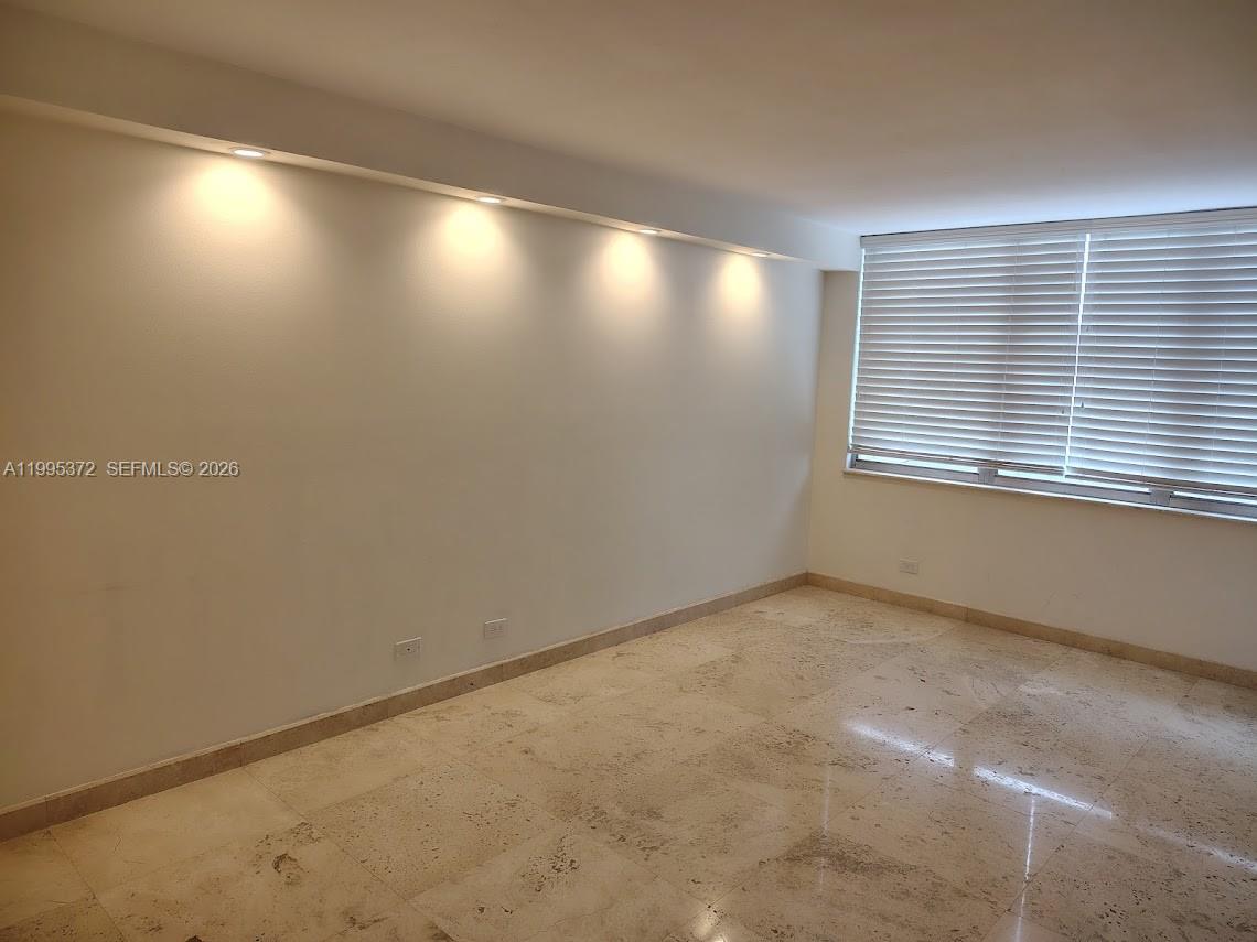 An empty room features light-colored marble flooring, recessed ceiling lighting, and windows with white blinds — 6039 Collins Ave # 407, Miami Beach FL 33140, MIAMI BEACH, FL