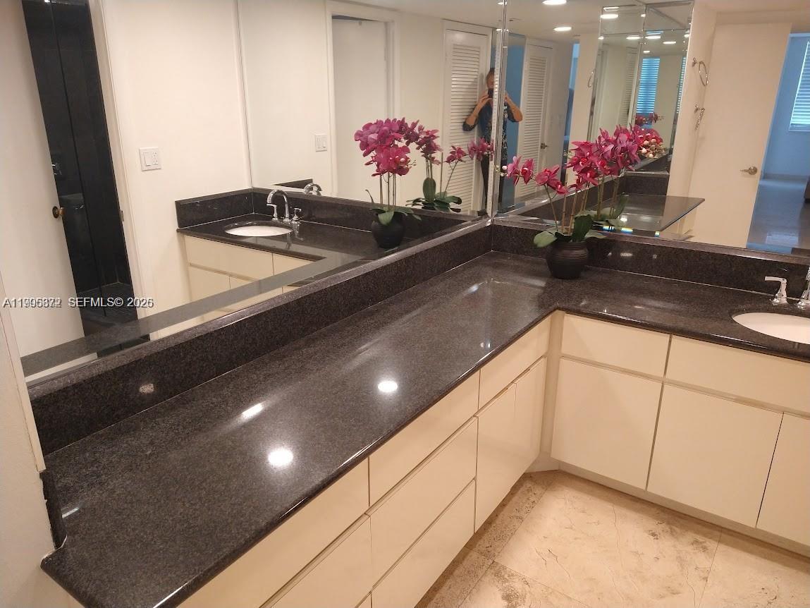 A bathroom features a dark granite countertop with dual sinks and white cabinetry — 6039 Collins Ave # 407, Miami Beach FL 33140, MIAMI BEACH, FL