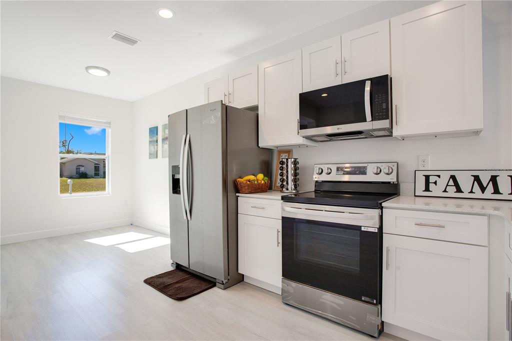 A modern kitchen features white cabinets, stainless steel appliances, and light-colored flooring — 10452 PENDLETON AVENUE, ENGLEWOOD, FL