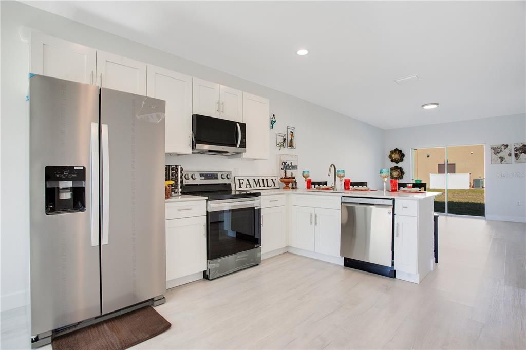 A kitchen with white cabinets, stainless steel appliances, and light wood-look flooring — 10452 PENDLETON AVENUE, ENGLEWOOD, FL