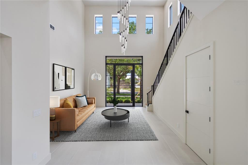 A modern, high-ceilinged foyer features a leather sofa, a circular coffee table, and a staircase — 737 N SUMMERLIN AVENUE, ORLANDO, FL