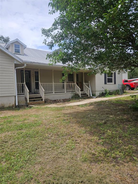 A tan, single-story house features a covered front porch with white railings and a metal roof — 18890 SW 44TH STREET, DUNNELLON, FL