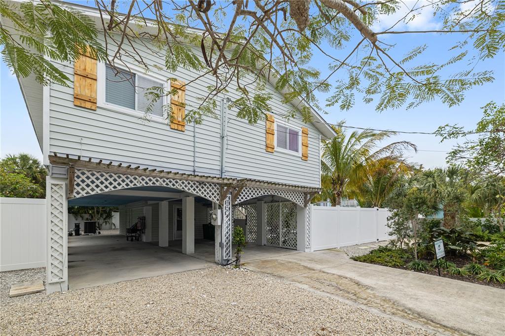 A two-story house on stilts features light blue siding, wooden shutters, and a covered parking area — 228 GLADIOLUS STREET, ANNA MARIA, FL
