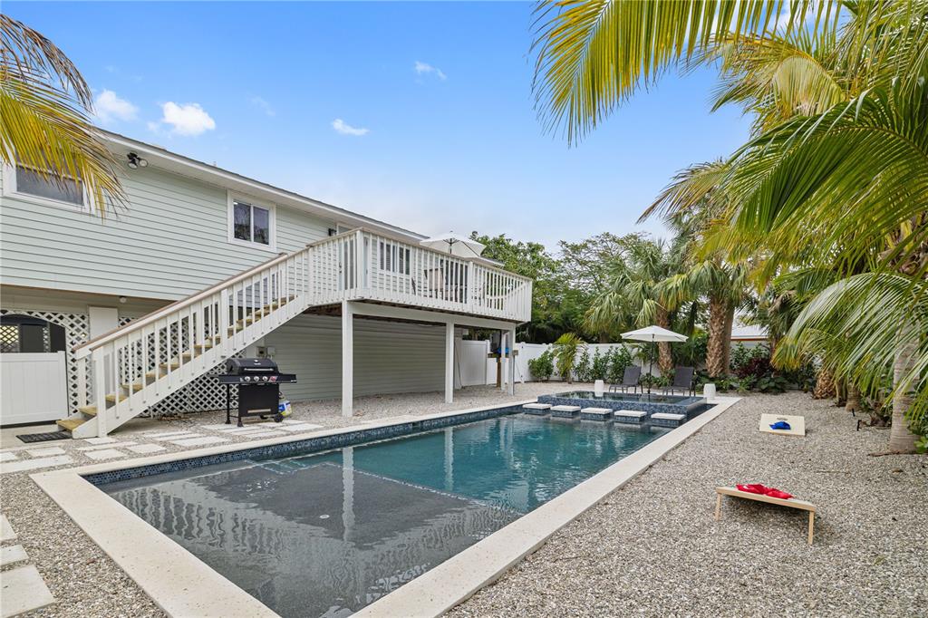 A backyard features a rectangular swimming pool with a sun shelf and an elevated wooden deck — 228 GLADIOLUS STREET, ANNA MARIA, FL