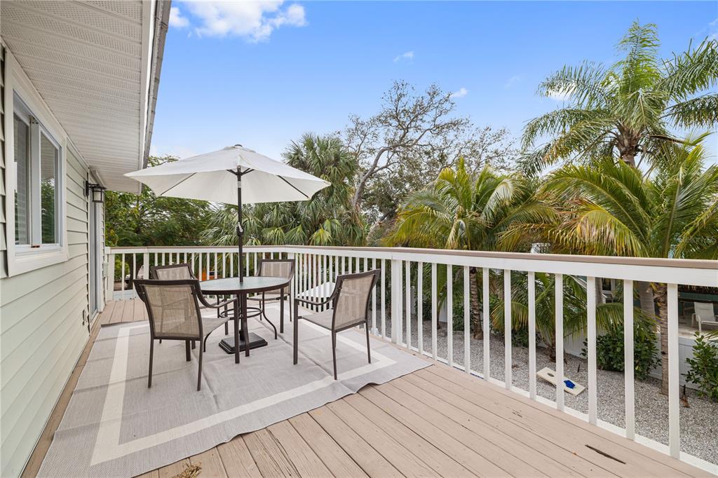 A wooden deck features a dining set with an umbrella and white railings outdoors — 228 GLADIOLUS STREET, ANNA MARIA, FL