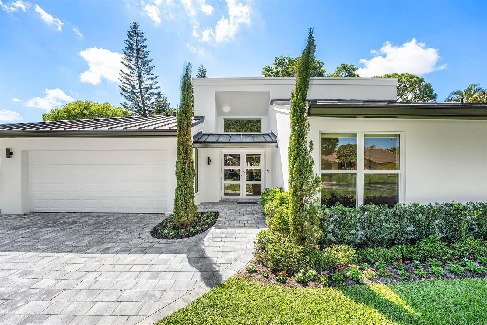 A modern white house features a paved driveway, a double front door, and tall cypress trees — 654 W Lakewoode Circle, Delray Beach FL 33445, DELRAY BEACH, FL
