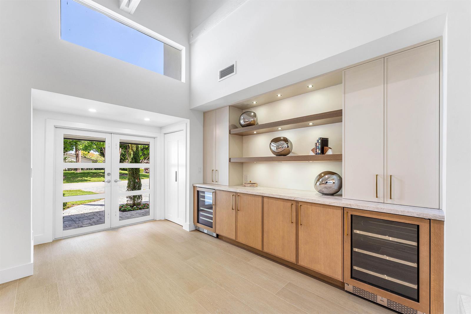 A modern wet bar with wood cabinets and two wine coolers sits near a glass entryway — 654 W Lakewoode Circle, Delray Beach FL 33445, DELRAY BEACH, FL