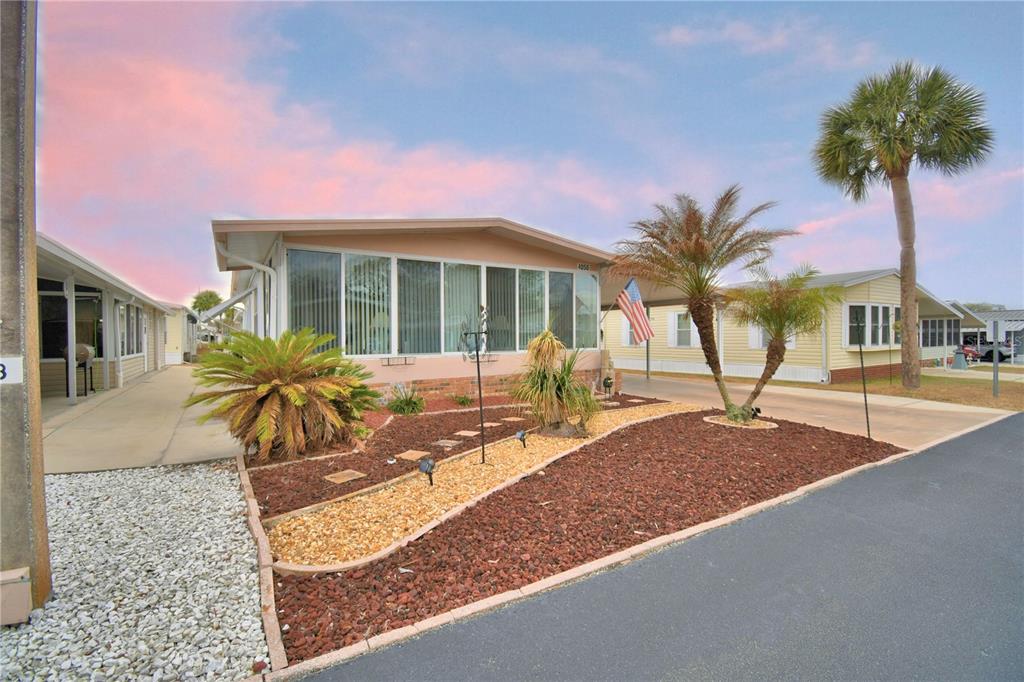 A single-story mobile home with a sunroom, carport, and landscaped yard under a sunset sky — 4056 ROLLING OAKS DRIVE, WINTER HAVEN, FL