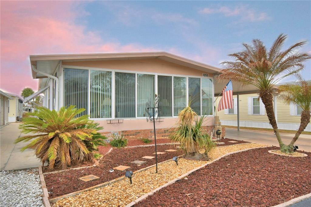 A single-story manufactured home with a glass-enclosed porch, carport, and landscaped front yard — 4056 ROLLING OAKS DRIVE, WINTER HAVEN, FL