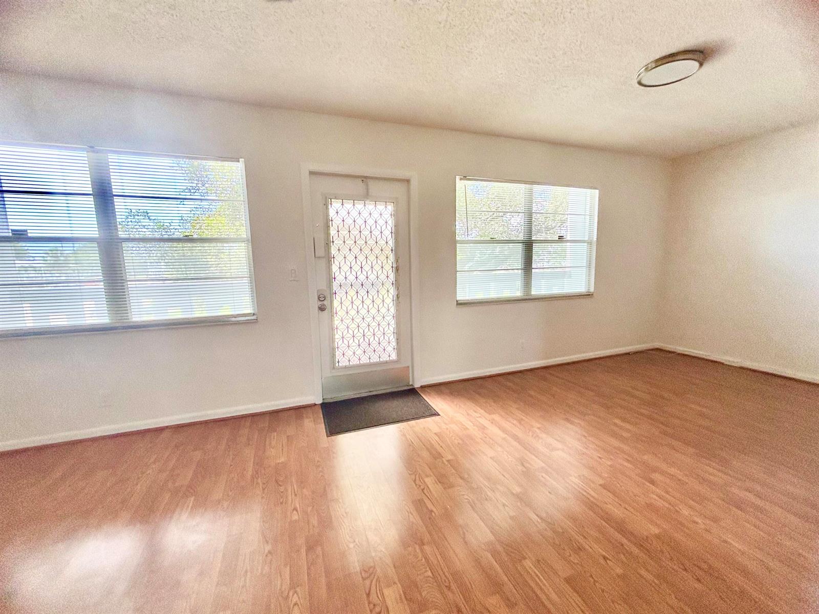An empty room features wood-look flooring, white walls, two windows with blinds, and a door — 2069 Oakridge F Unit 2069, Deerfield Beach FL 33442, DEERFIELD BEACH, FL