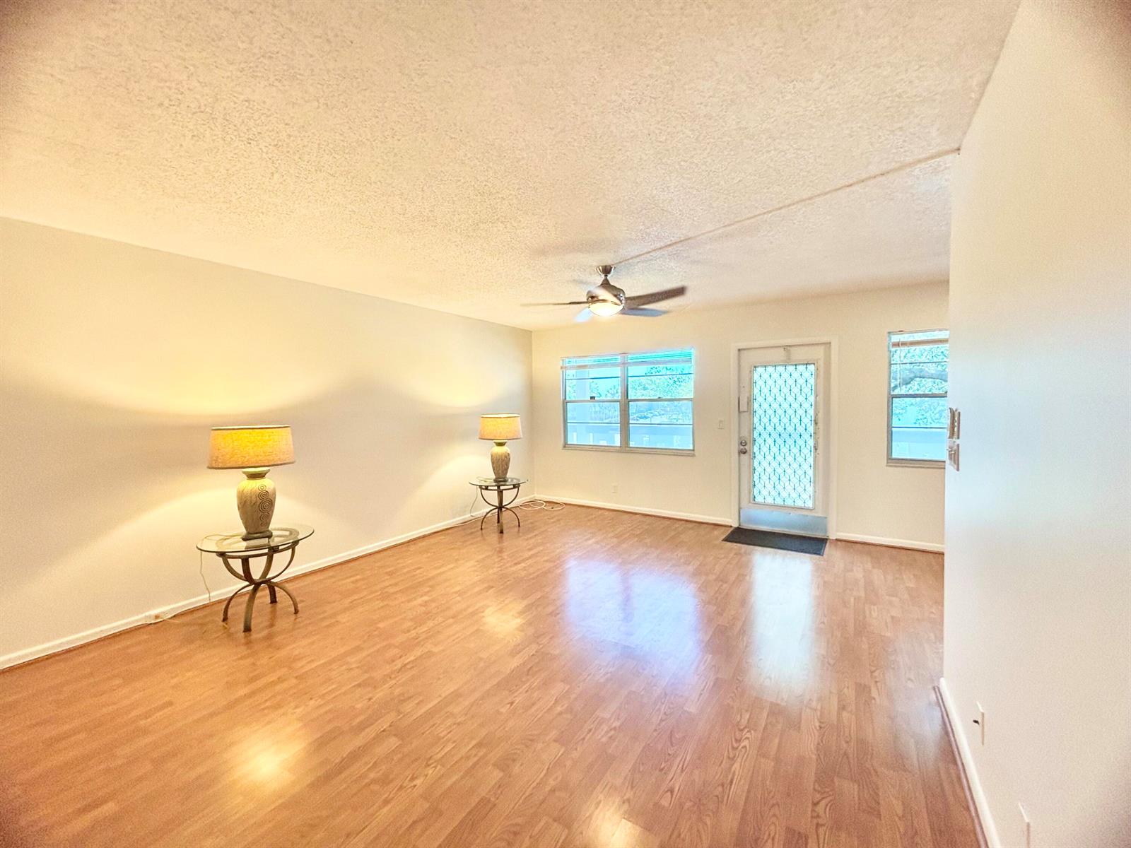 An empty living room features wood-look flooring, a ceiling fan, and two glass-topped side tables — 2069 Oakridge F Unit 2069, Deerfield Beach FL 33442, DEERFIELD BEACH, FL